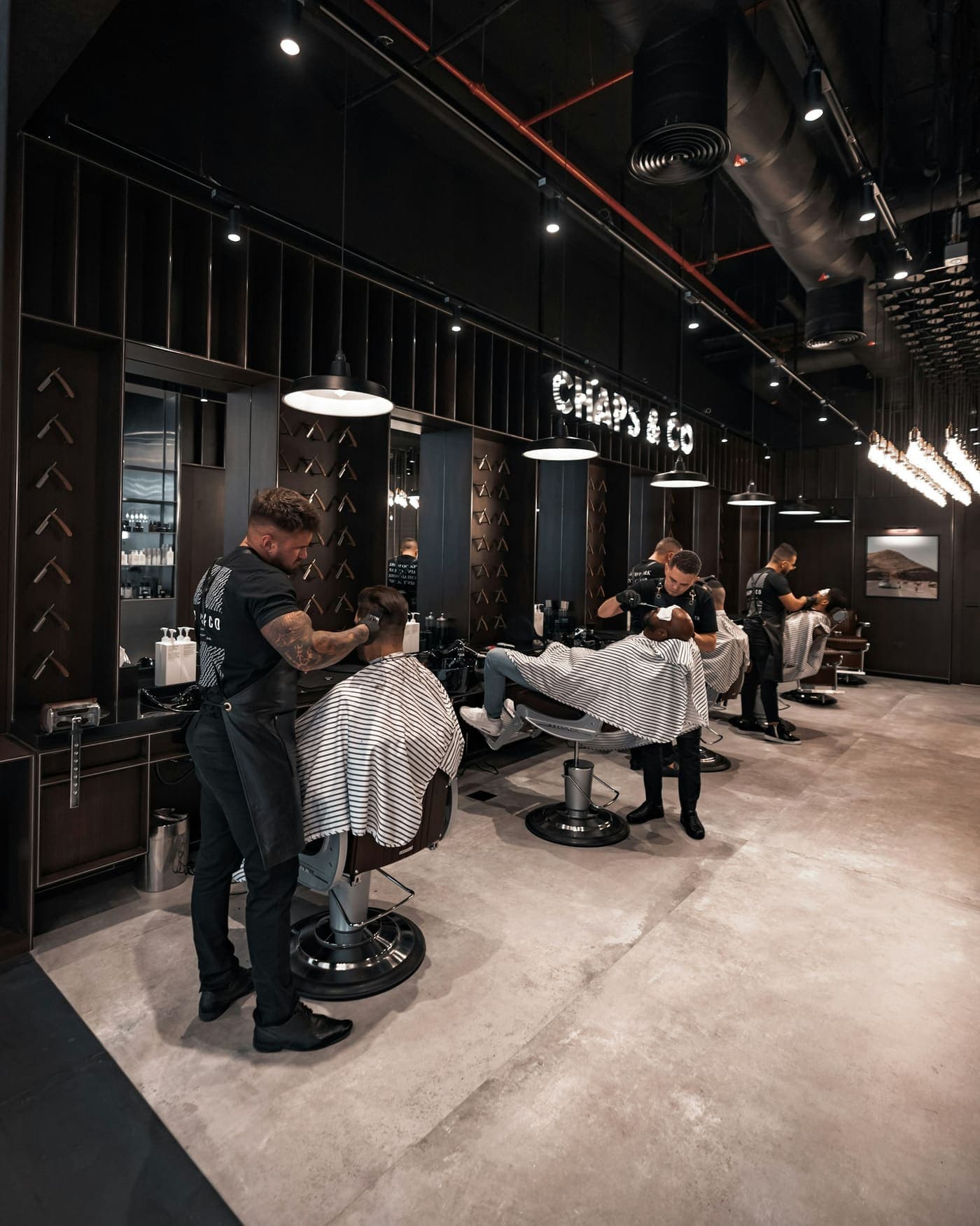 Interior de una barbería con varios sillones atendiendo clientes a la vez
