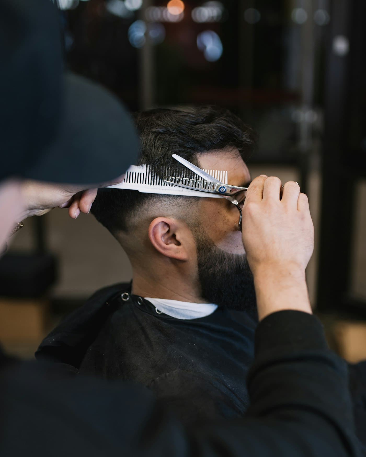 Barbero cortando el pelo con tijera y peine a un cliente