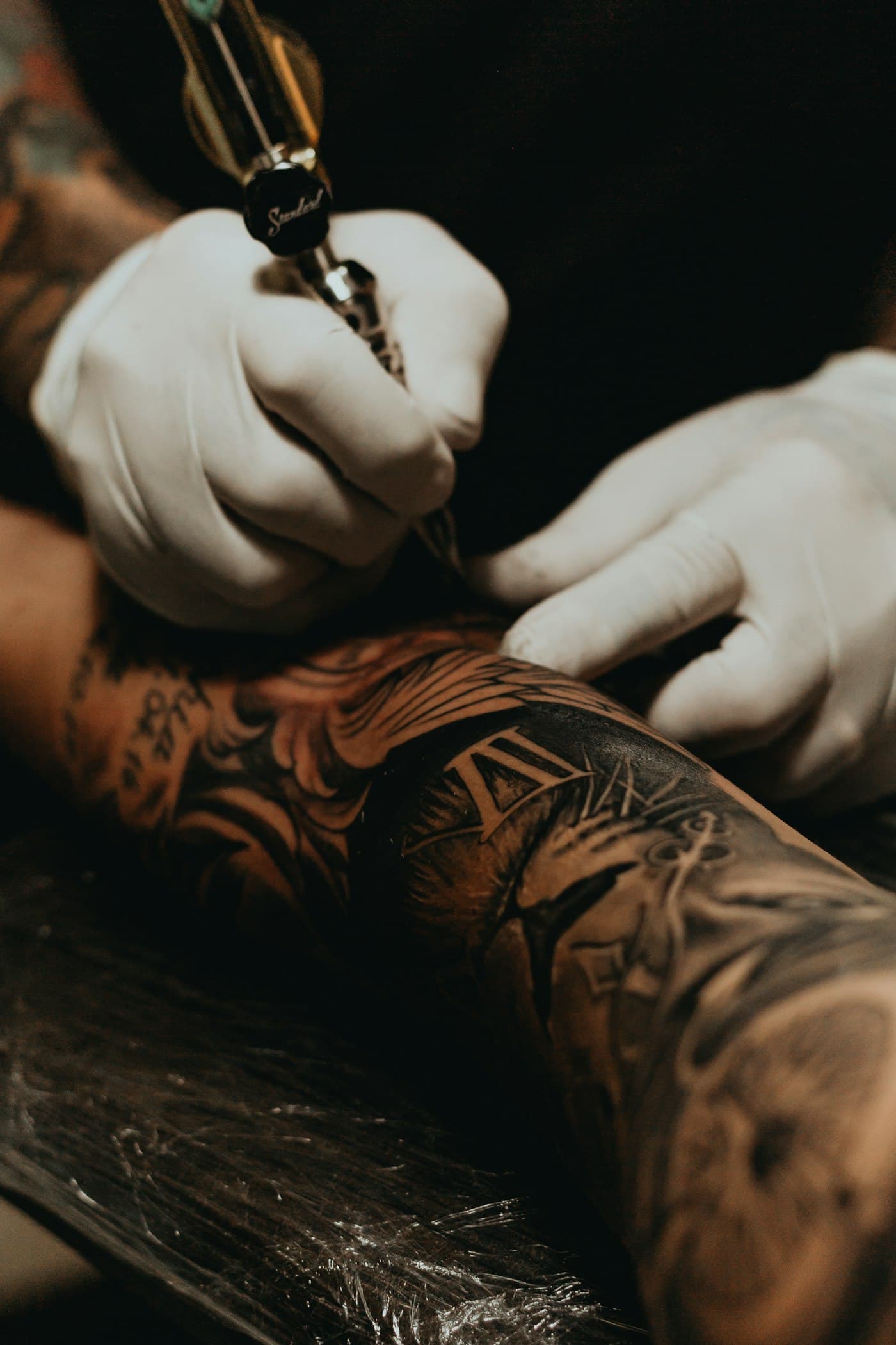 Tatuador trabajando en el brazo de un cliente con guantes negros